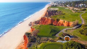 Ein Golfplatz an der Küste mit Strand, Klippen und einem Wohngebiet im Hintergrund.