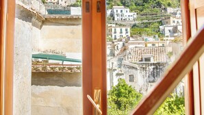 A view from a room with a wooden door leading to a balcony, overlooking a hillside with buildings and a castle-like structure.