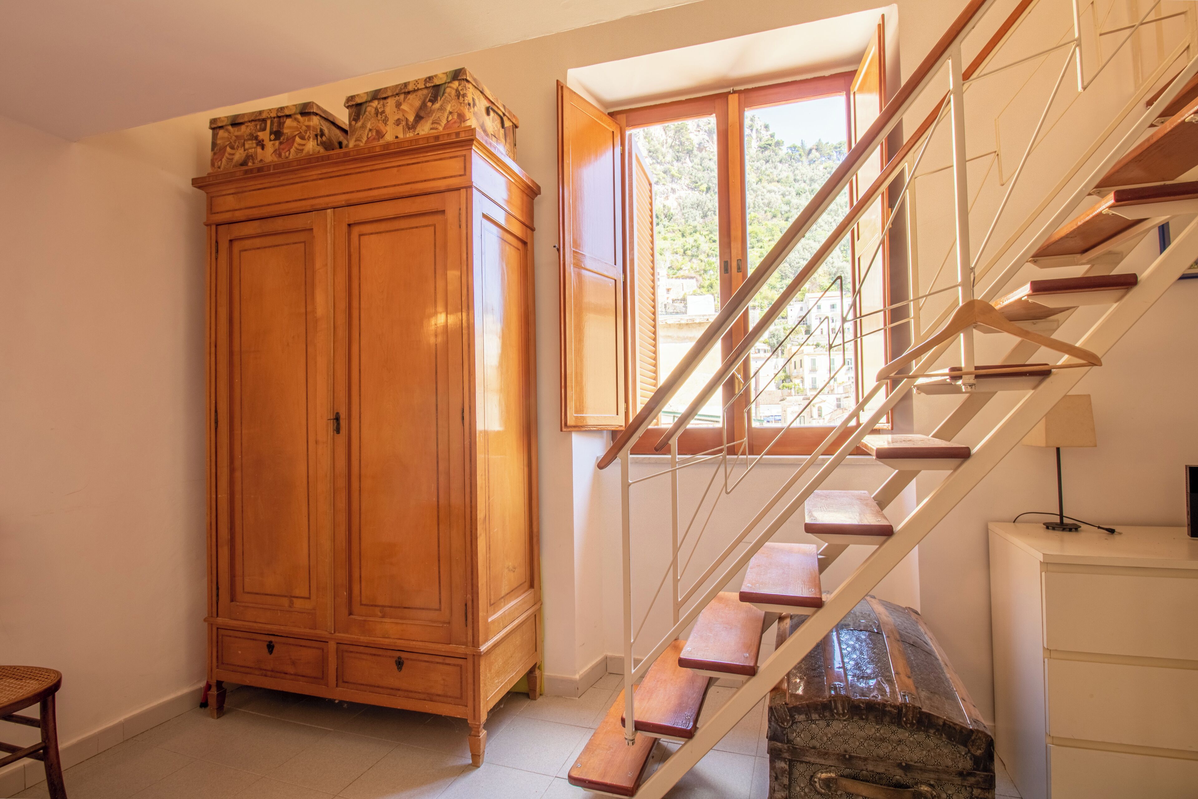 Eine Treppe mit Holzboden und Metallgeländern, ein Holzschrank und ein Fenster mit geöffneten Fensterläden.