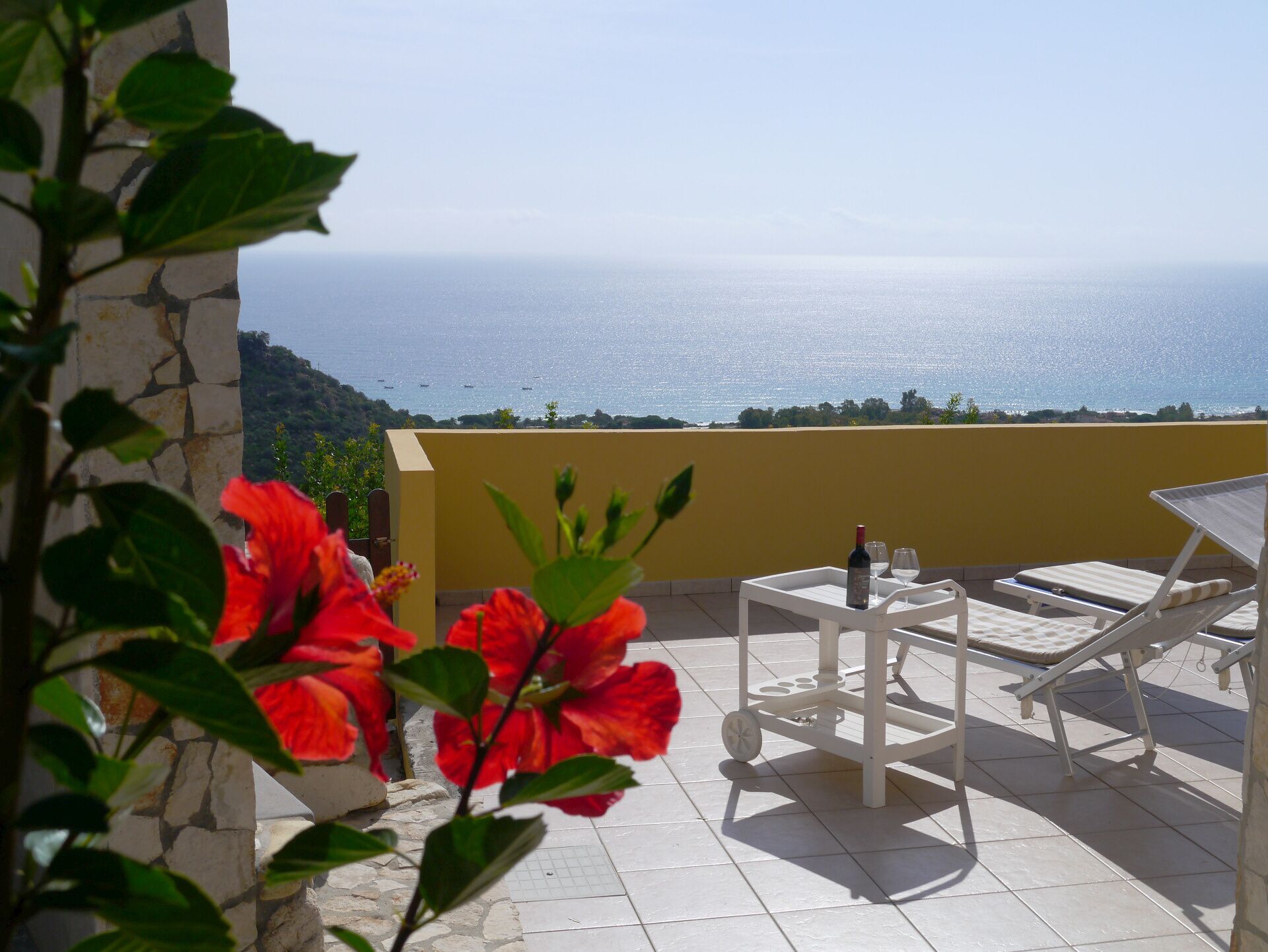 Une terrasse avec une table et des chaises, une bouteille de vin et une vue sur la mer.