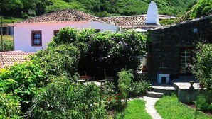Um cenário rural com um edifício de pedra, uma casa cor-de-rosa e um caminho de jardim.