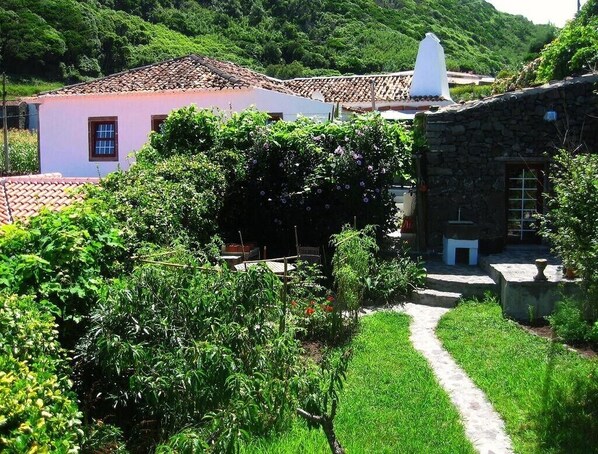 Entorno rural con una construcción de piedra, una casa rosa y un sendero de jardín.