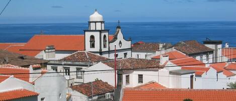 Un pueblo costero con edificios blancos y tejados rojos, una iglesia destacada con un campanario, y el mar al fondo.