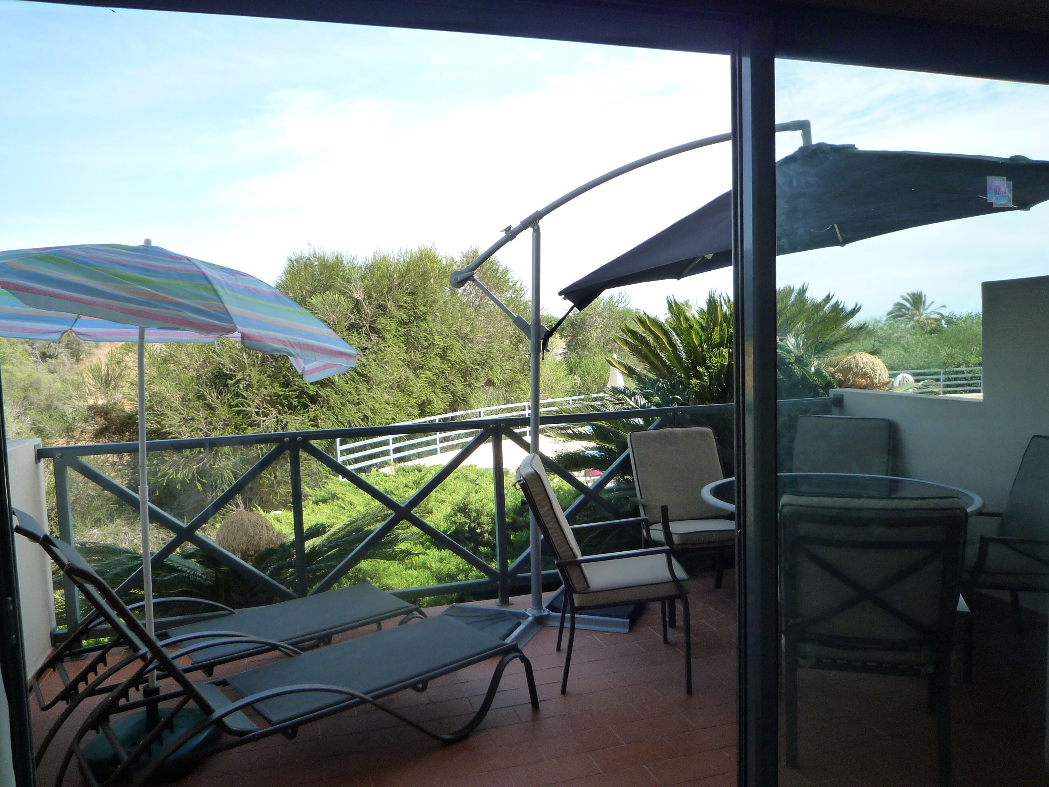 A balcony with two sun loungers, a table, and a striped umbrella.