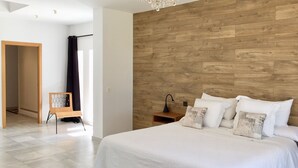 Un dormitorio con cabecera de madera, una cama grande con ropa de cama blanca, una araña y una mesita de noche con lámpara.