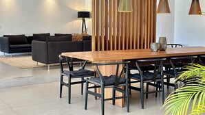 Un comedor moderno con una mesa y sillas de madera, un sofá negro y un alto separador de madera.