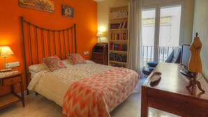 Une chambre à coucher comprenant un lit, une table de chevet, une lampe, une bibliothèque et donnant sur le balcon extérieur.
