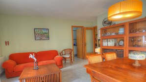 Un salon avec un canapé rouge, une table basse en bois, une table à manger et des chaises. On y trouve également une bibliothèque remplie de livres et d’objets décoratifs.