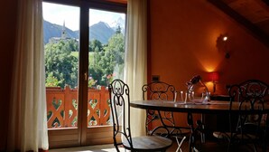A dining area with a table and chairs, a view of a mountain and a church through a large window, and a red wall. - Chalet with a beautiful view to comfortably enjoy nature in the Park and Valley (Introd)