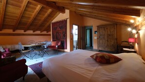 A spacious bedroom with a large bed, a wooden ceiling, a dining table with chairs, and a red chair. - Chalet with a beautiful view to comfortably enjoy nature in the Park and Valley (Introd)