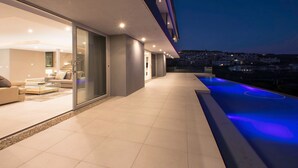 Een modern huis met een ruime balkon, een goed verlicht interieur en uitzicht op de stad in de schemering.