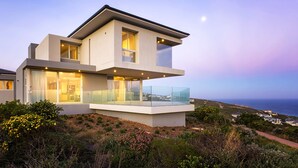 Een modern herenhuis met twee verdiepingen, grote glasramen en een balkon, met uitzicht op een kustlandschap.