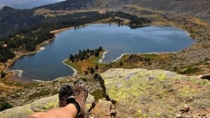 A panoramic view of a lake surrounded by mountains, with a person's feet visible on a rocky outcrop. - Casa Rural Bocanegra for 2 people (Canicosa de la Sierra)