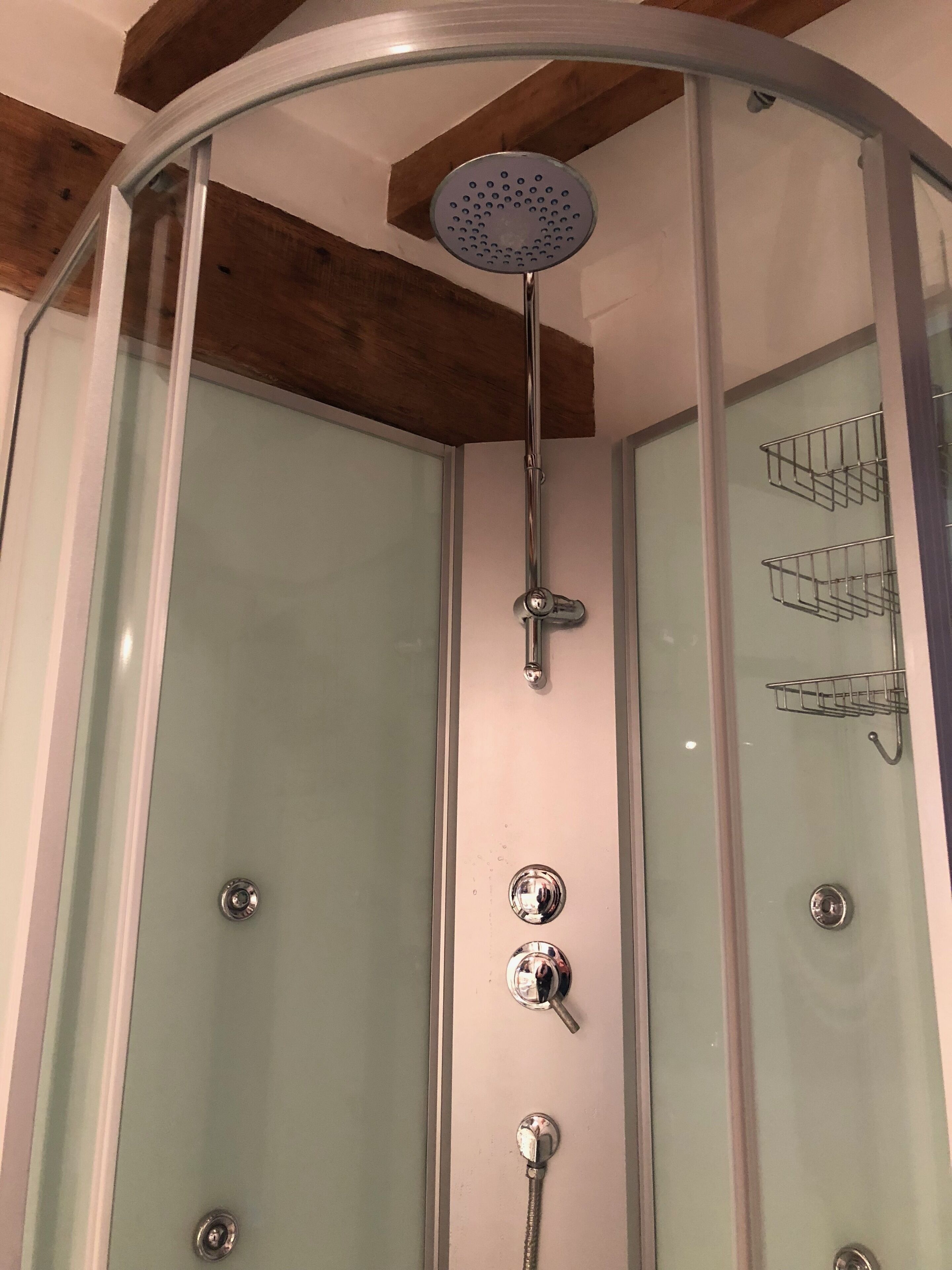 A glass-enclosed shower with a handheld showerhead, a wall-mounted control panel, and a towel rack.
