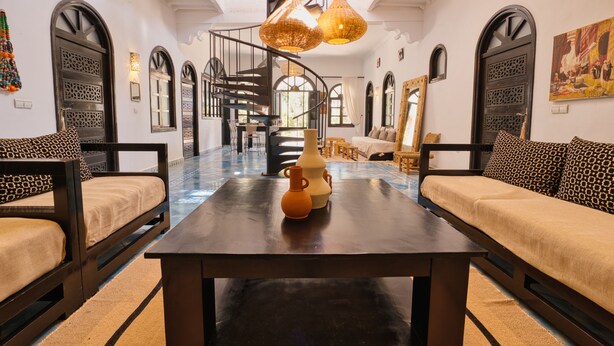 Ein geräumiges Zimmer mit einem zentralen Tisch, zwei Sofas, einer Wendeltreppe und dekorativer Beleuchtung.