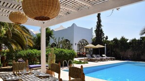 Ein Essbereich am Pool mit Korbstühlen, einem für eine Mahlzeit gedeckten Tisch und einem Pool mit Liegestühlen.