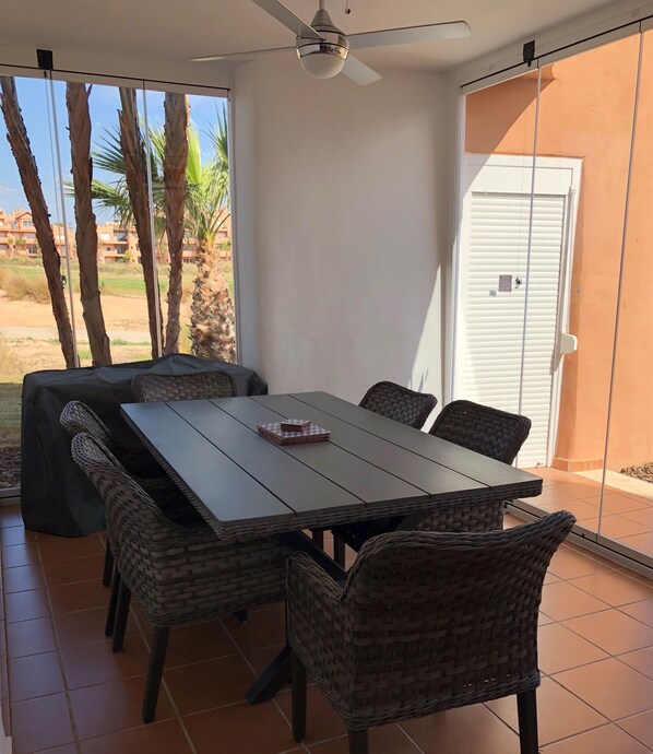 A dining area with a table and chairs, a ceiling fan, and a view of palm trees and buildings.