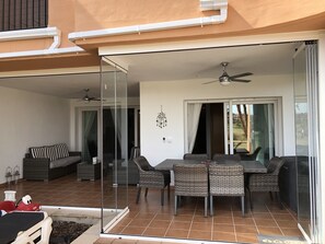 Un balcon avec une porte vitrée, un ventilateur de plafond, une table à manger avec des chaises en osier et un canapé.