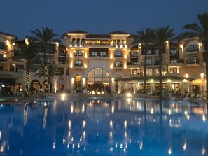 A hotel with a large pool, multiple balconies, and a central archway.