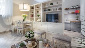 A modern living room with a dining area, white cabinetry, a flat-screen TV, and a kitchen area with a sink and countertop.