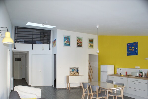 A modern kitchen with a dining area, featuring a white fridge, a yellow wall, and a ceiling light.