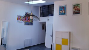Ett rum med ett vitt element, en hängande lampa, en dörr och en gul och vit förvaringsmöbel.