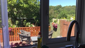A view from a window overlooking a wooden deck with wicker furniture and potted plants. - Gower coast bungalow (Swansea City)