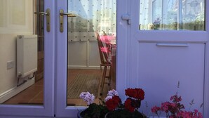A conservatory with a glass door, a radiator, and a chair visible through the door. - Gower coast bungalow (Swansea City)