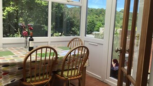 A conservatory with a tiled floor, a table with a colorful tablecloth, two wooden chairs, and a bottle of wine. - Gower coast bungalow (Swansea City)