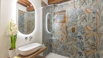 A bathroom with a large oval sink, a mirror, and a shower area with a floral tile design.