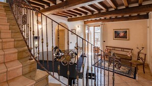 A grand staircase with a wrought iron railing leading to a living area with a piano, a bench, and a painting on the wall. - Corte della Luna, elegant villa with swimming pool surrounded by a suggestive olive grove (Cortona)
