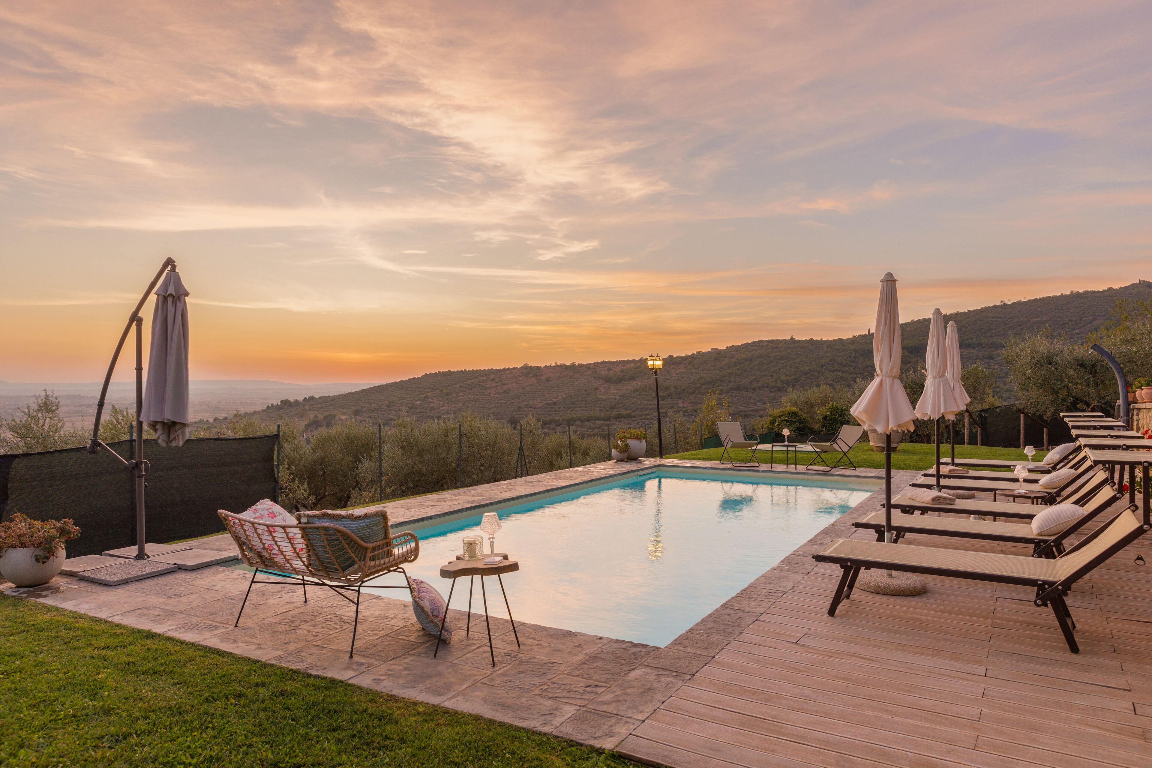 A swimming pool with lounge chairs and umbrellas, surrounded by a deck and a view of hills.
