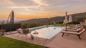 A swimming pool with lounge chairs and umbrellas, surrounded by a deck and a view of hills. - Corte della Luna, elegant villa with swimming pool surrounded by a suggestive olive grove (Cortona)