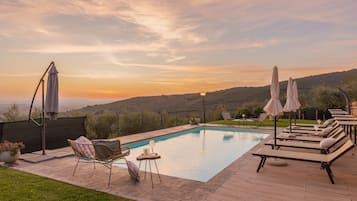 A swimming pool with lounge chairs and umbrellas, surrounded by a deck and a view of hills.