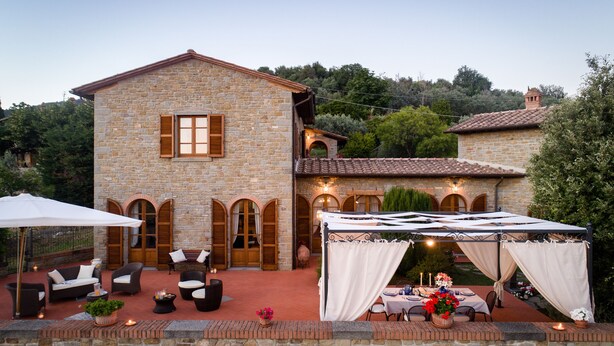 A stone building with a terrace, outdoor seating, and a tented dining area. - Corte della Luna, elegant villa with swimming pool surrounded by a suggestive olive grove (Cortona)