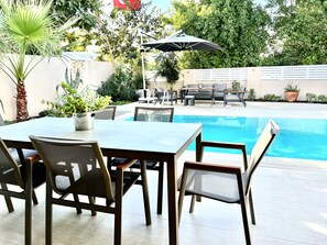 Un espace aménagé au bord de la piscine, avec une table et des chaises, un fauteuil de relaxation et une petite table sur laquelle est posée une plante en pot.