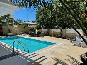 A swimming pool with a sunshade, surrounded by outdoor furniture and potted plants.