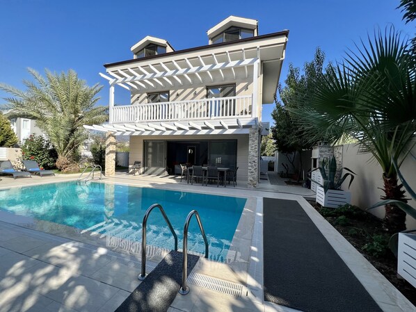 Une maison à deux étages avec une piscine, du mobilier d’extérieur et un patio couvert.