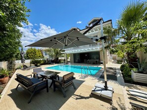Un espace piscine doté d’un coin salon couvert, de chaises longues et d’une table.