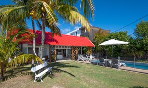 Un espace aménagé au bord de la piscine, avec des chaises longues, un banc blanc et un bâtiment doté d’un toit rouge.