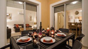 Un coin repas avec une table en verre, des chaises en osier noir et une vue sur le salon grâce à des portes vitrées.
