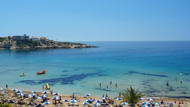 Une plage avec une eau d’un bleu limpide, des parasols et des gens.