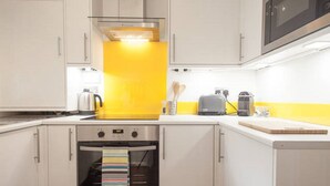 Una cocina moderna con armarios blancos, un salpicadero amarillo y electrodomésticos de acero inoxidable, incluyendo un microondas, tostadora y hervidor.