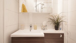 Un baño con lavamanos blanco, un espejo, toallero, ducha y una planta en maceta.