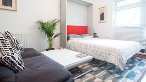 Una habitación compacta con cama, sofá, una mesita y una planta en maceta.