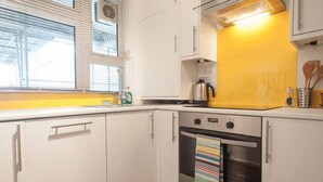 Una cocina con gabinetes blancos, salpicadero amarillo, estufa y ventana con persianas.