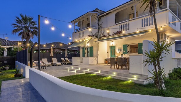 A two-story house with a balcony, outdoor seating area, and string lights.