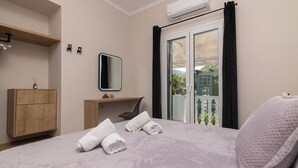 A bedroom with a bed, a wooden dresser, a desk, a mirror, and a balcony with a view.