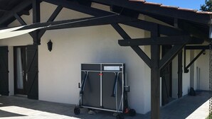 Un espacio al aire libre cubierto con un carrito metálico, una chimenea y un edificio de techo con tejas y vigas de madera.