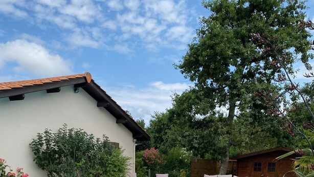 Una piscina rectangular con cubierta de madera, un edificio blanco con techo marrón y una cabaña de madera al fondo.